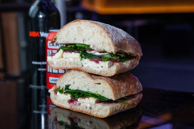 A ciabatta sandwich with a beer and wine bottle in the background